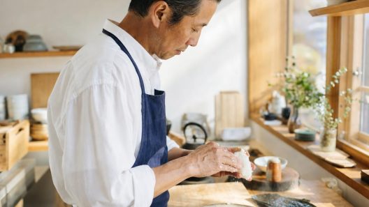Chef japonais façonnant un onigiri triangulaire à la main dans une cuisine