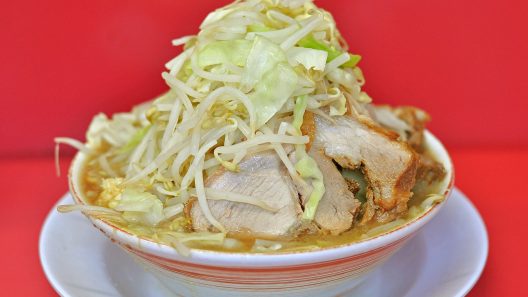 Bol de ramen de style Jiro couronné d'une montagne de moyashi et de chou, avec des tranches de porc